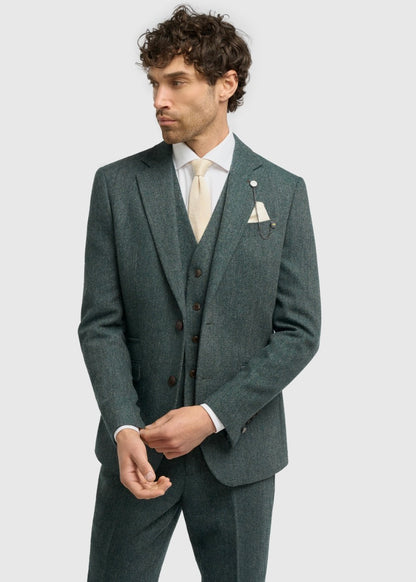 Man wearing a teal suit with a white shirt and beige tie on a light grey background
