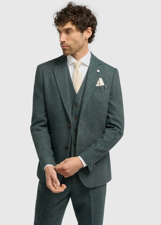 Man wearing a teal suit with a white shirt and beige tie on a light grey background